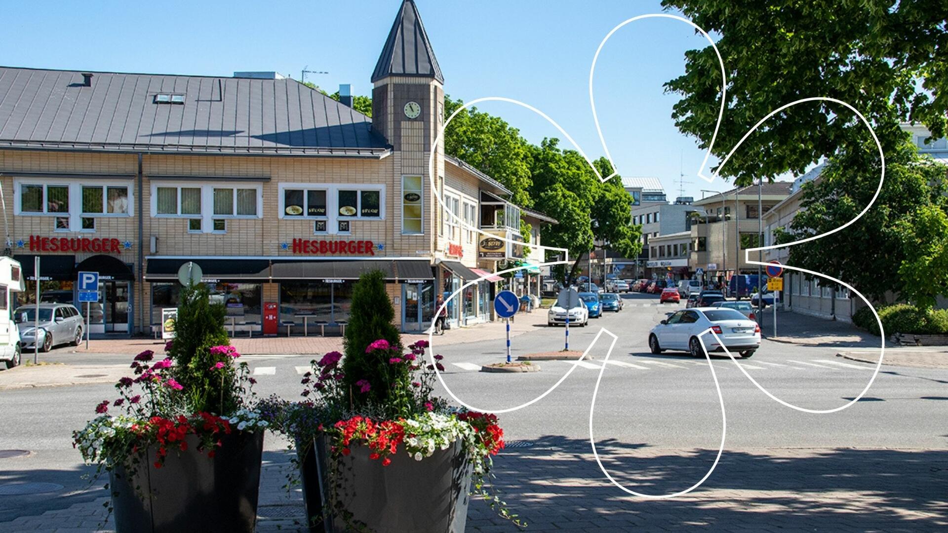 Tullikadun, Kaivokadun ja Uolevi Raaden kadun risteys, etualalla kesäkukkaistutuksia isossa ruukussa. Kuvan päällä Onnellinen aurinko -symboli.
