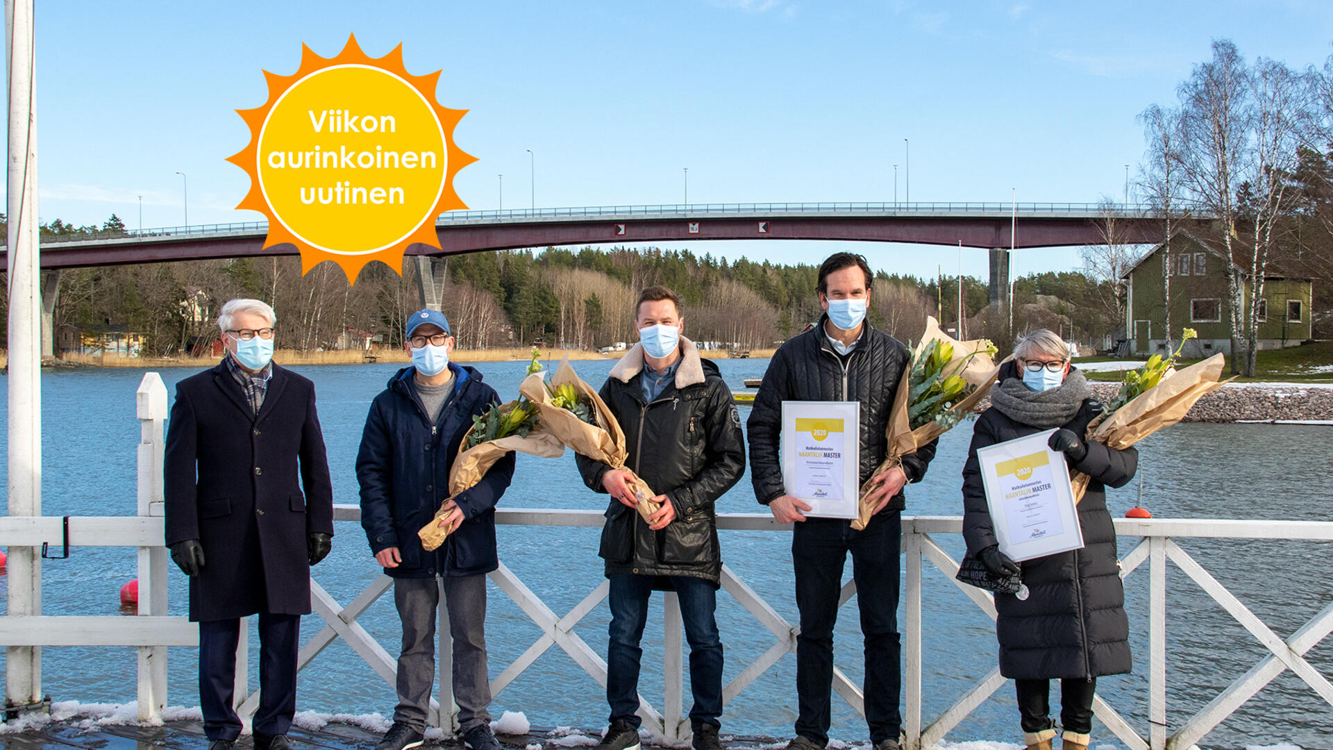 Kaupunginjohtaja Jouni Mutanen, Rantamakasiinin kolme pitäjää ja Tiina Tunturi seisovat rivissä maskit kasvoillaan, palkintokukat ja -stidendit käsissään merimaiseman edessä.